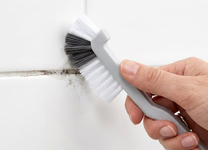 Hand using a cleaning brush to remove grime from a tile joint, with WSGenie branding.